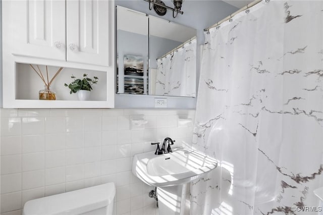 bathroom with toilet, sink, and tile walls