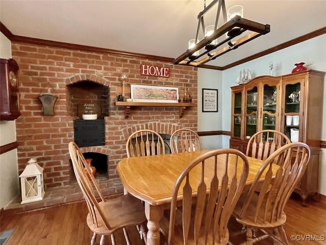 dining space with hardwood / wood-style flooring, ornamental molding, a fireplace, and a notable chandelier