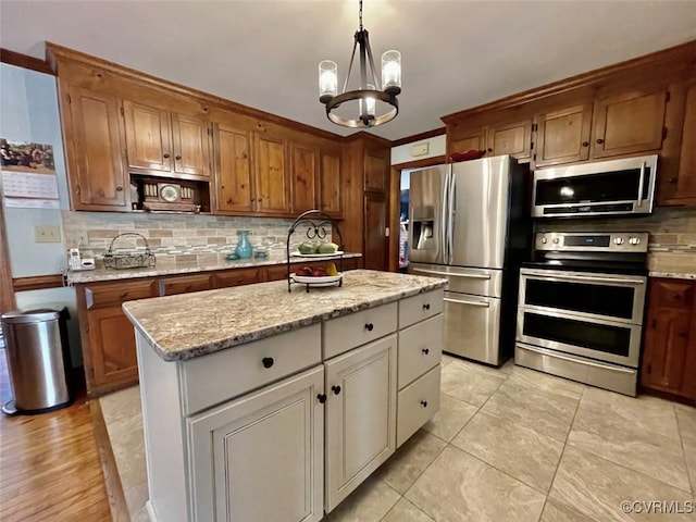 kitchen with pendant lighting, an inviting chandelier, stainless steel appliances, a center island, and light stone countertops