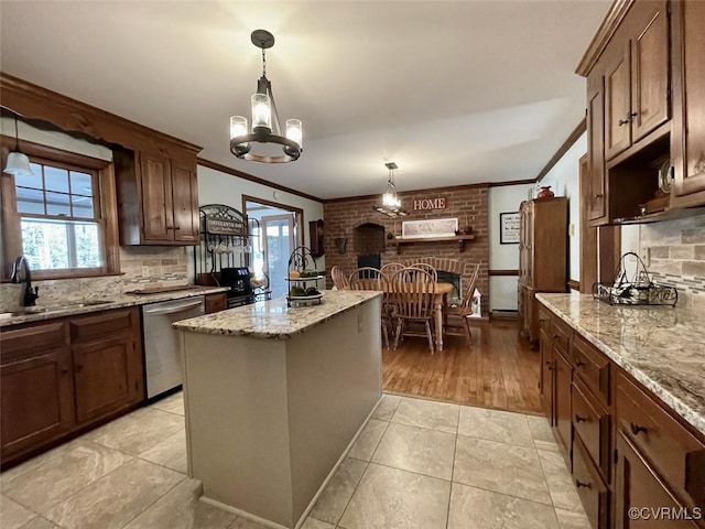 kitchen featuring sink, decorative light fixtures, a center island, stainless steel dishwasher, and light stone countertops