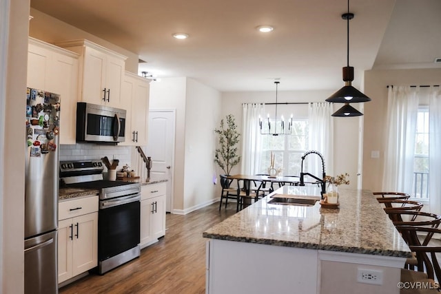 kitchen with hanging light fixtures, an island with sink, appliances with stainless steel finishes, and white cabinets