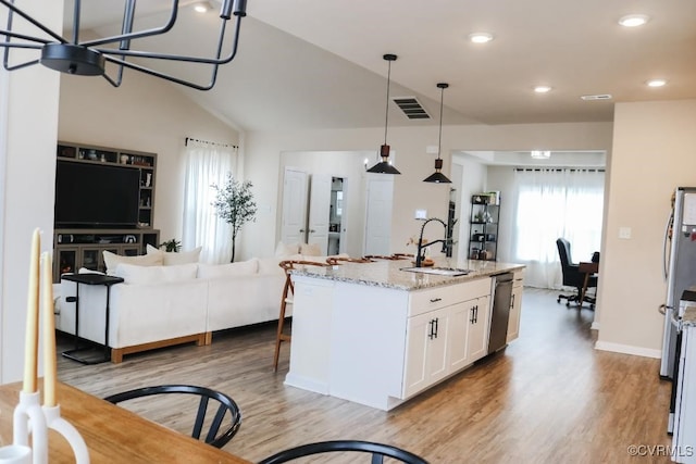 kitchen featuring decorative light fixtures, an island with sink, sink, white cabinets, and light stone countertops