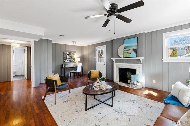 living room featuring crown molding, dark wood-type flooring, a premium fireplace, and ceiling fan