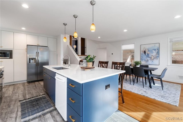 kitchen featuring blue cabinets, sink, appliances with stainless steel finishes, a kitchen island with sink, and white cabinets