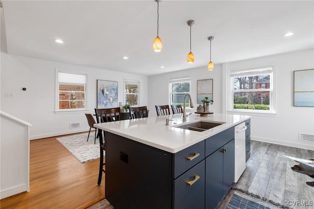 kitchen with blue cabinetry, sink, dishwasher, an island with sink, and pendant lighting