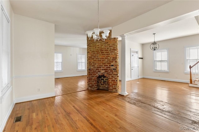 unfurnished living room featuring an inviting chandelier, hardwood / wood-style flooring, a fireplace, and decorative columns