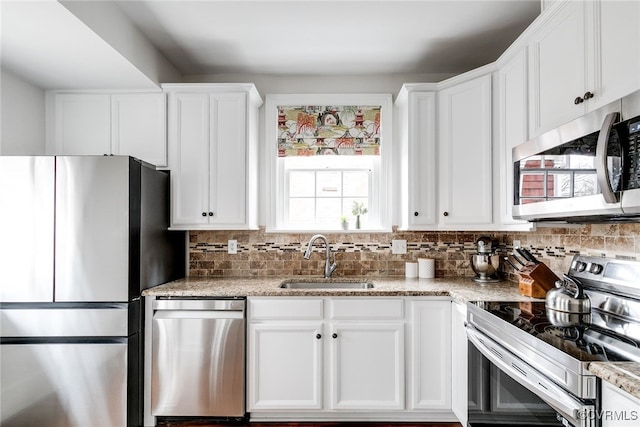 kitchen with sink, light stone counters, white cabinets, stainless steel appliances, and backsplash