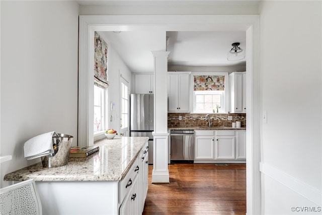 kitchen with light stone countertops, stainless steel appliances, white cabinets, and ornate columns