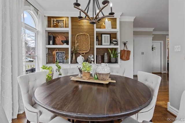 dining space with dark wood-type flooring, ornamental molding, built in shelves, and a notable chandelier