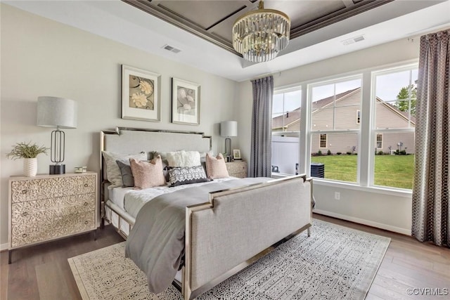 bedroom with a raised ceiling, wood-type flooring, crown molding, and a chandelier