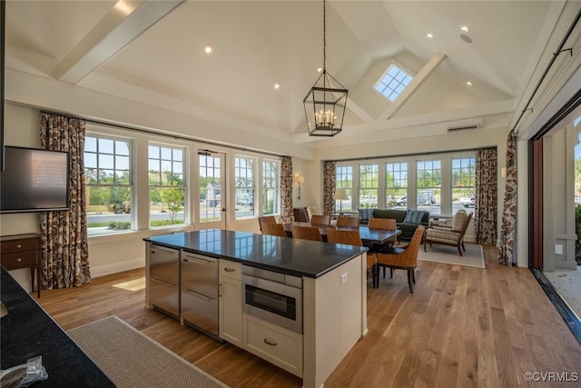 kitchen with hanging light fixtures, high vaulted ceiling, stainless steel microwave, white cabinets, and a chandelier