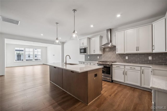 kitchen featuring pendant lighting, wall chimney range hood, stainless steel stove, white cabinetry, and built in microwave