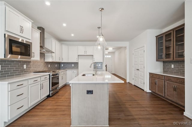 kitchen with stainless steel stove, built in microwave, sink, a kitchen island with sink, and wall chimney exhaust hood