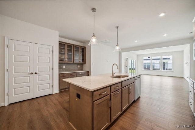 kitchen featuring dishwasher, sink, backsplash, a kitchen island with sink, and light stone countertops