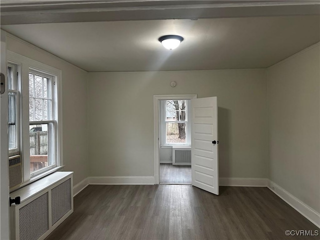 empty room featuring a wealth of natural light, radiator heating unit, and dark hardwood / wood-style flooring