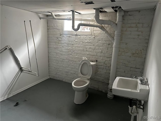 bathroom with sink, concrete flooring, toilet, and brick wall