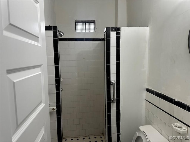 bathroom with tiled shower, toilet, and tile walls