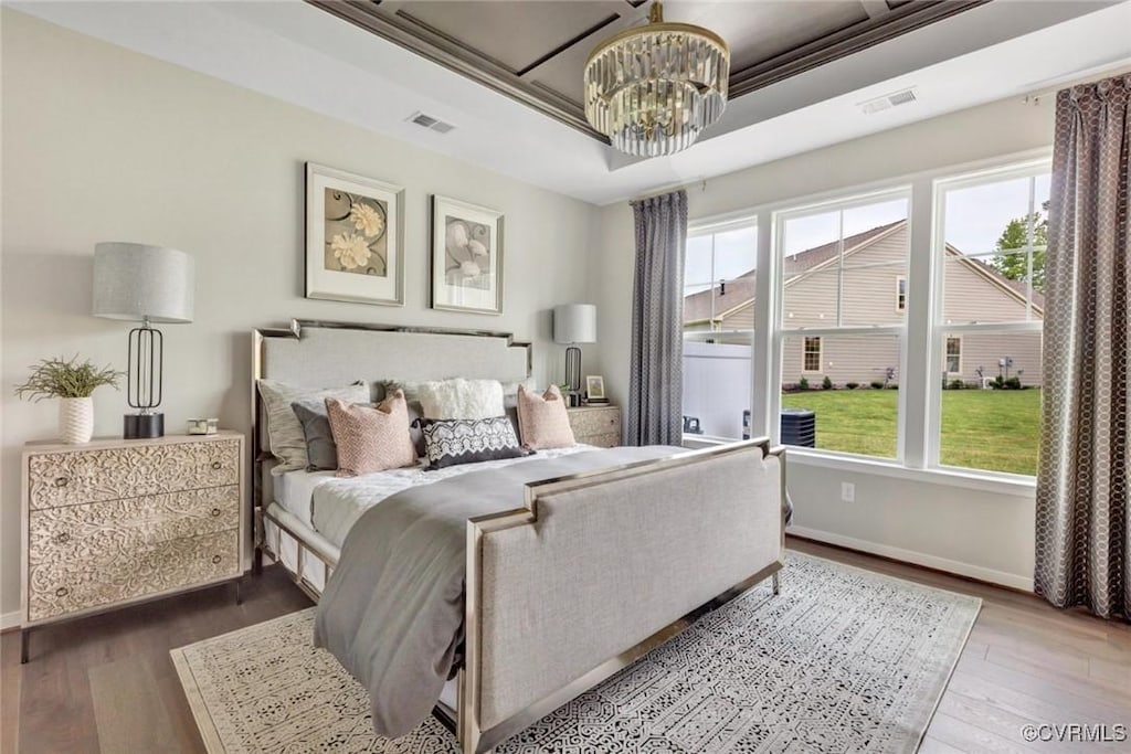 bedroom featuring a tray ceiling, hardwood / wood-style flooring, and a chandelier