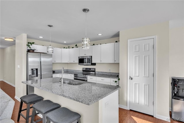 kitchen with white cabinetry, stainless steel appliances, decorative light fixtures, and an island with sink