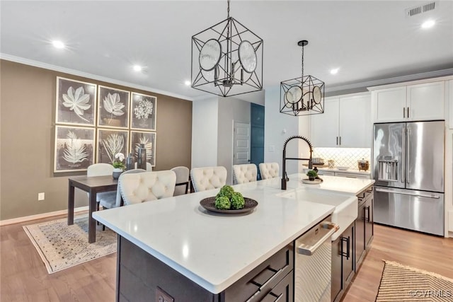 kitchen with appliances with stainless steel finishes, decorative light fixtures, sink, white cabinets, and a center island with sink