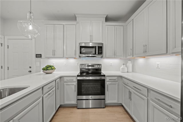 kitchen featuring appliances with stainless steel finishes, white cabinetry, tasteful backsplash, decorative light fixtures, and light wood-type flooring