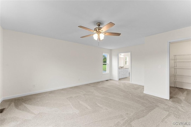 unfurnished bedroom featuring ceiling fan, ensuite bathroom, a walk in closet, light colored carpet, and a closet