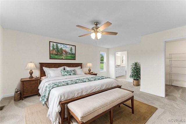 carpeted bedroom with ensuite bath, a walk in closet, a closet, and ceiling fan