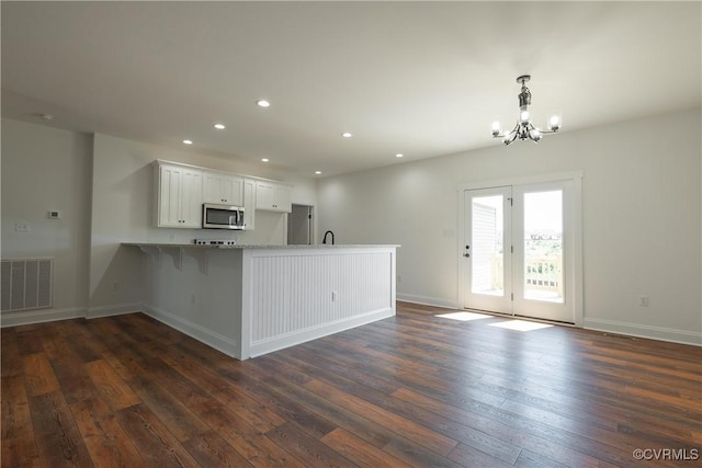 kitchen with decorative light fixtures, dark hardwood / wood-style flooring, a kitchen breakfast bar, kitchen peninsula, and white cabinets