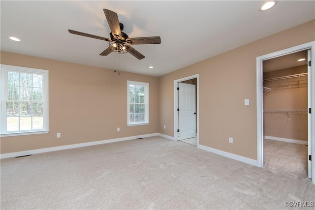 unfurnished bedroom featuring ceiling fan, a spacious closet, light carpet, and multiple windows