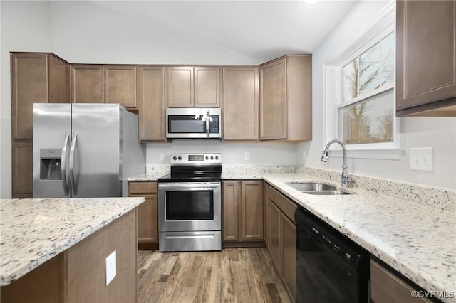 kitchen featuring sink, vaulted ceiling, light hardwood / wood-style flooring, stainless steel appliances, and light stone countertops