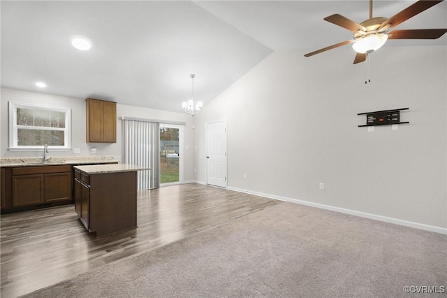 kitchen with sink, light stone counters, vaulted ceiling, a kitchen island, and pendant lighting