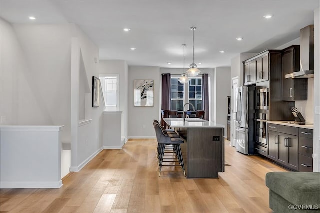 kitchen featuring a kitchen bar, decorative light fixtures, a center island with sink, stainless steel appliances, and wall chimney range hood