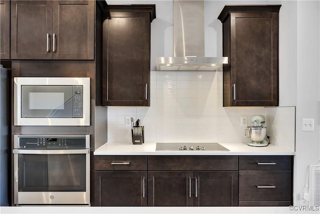 kitchen with dark brown cabinetry, backsplash, stainless steel appliances, and wall chimney exhaust hood