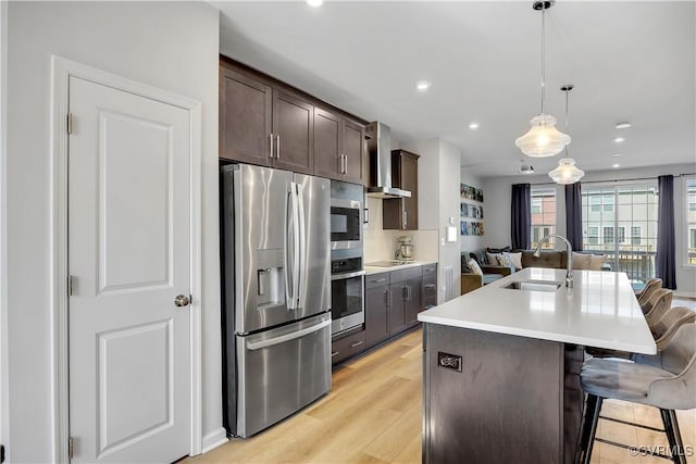 kitchen featuring pendant lighting, sink, wall chimney range hood, stainless steel fridge, and a kitchen bar