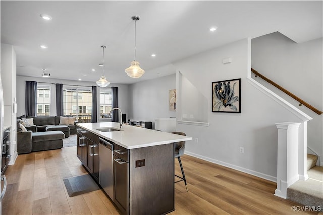 kitchen with dark brown cabinetry, sink, stainless steel dishwasher, pendant lighting, and a kitchen island with sink