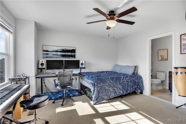 bedroom featuring ceiling fan, light colored carpet, and ensuite bath