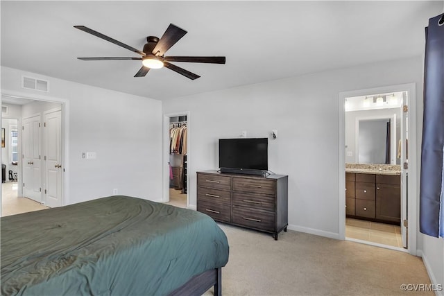 bedroom with ensuite bathroom, a walk in closet, light carpet, a closet, and ceiling fan