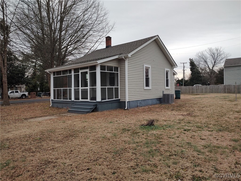 view of side of home with central AC unit, a yard, and a sunroom