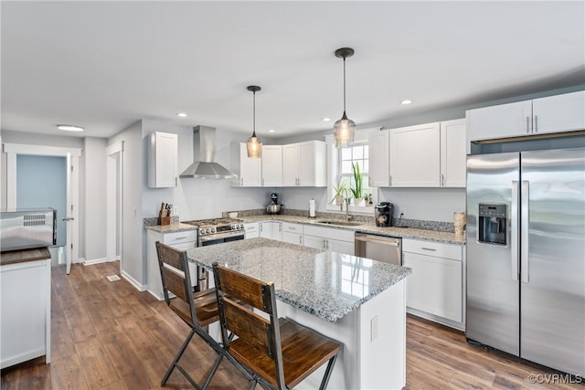 kitchen with white cabinets, hanging light fixtures, a center island, stainless steel appliances, and wall chimney exhaust hood