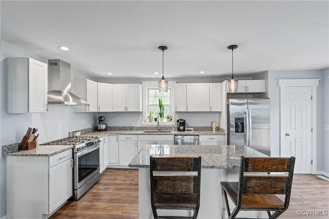 kitchen featuring wall chimney exhaust hood, sink, a center island, hanging light fixtures, and appliances with stainless steel finishes