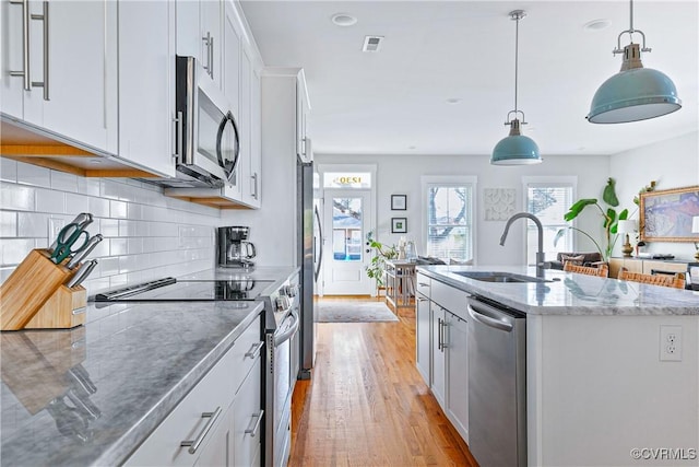 kitchen with appliances with stainless steel finishes, pendant lighting, white cabinetry, sink, and a kitchen island with sink