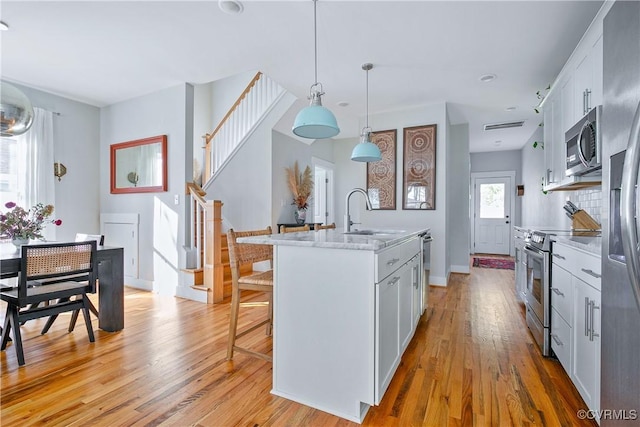 kitchen with sink, appliances with stainless steel finishes, white cabinets, a center island with sink, and decorative light fixtures