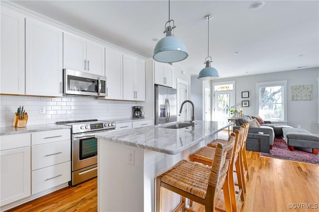 kitchen featuring sink, light stone counters, decorative light fixtures, a center island with sink, and stainless steel appliances