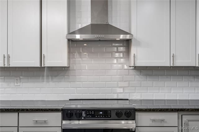 kitchen with stainless steel range with electric stovetop, tasteful backsplash, white cabinets, dark stone counters, and wall chimney exhaust hood