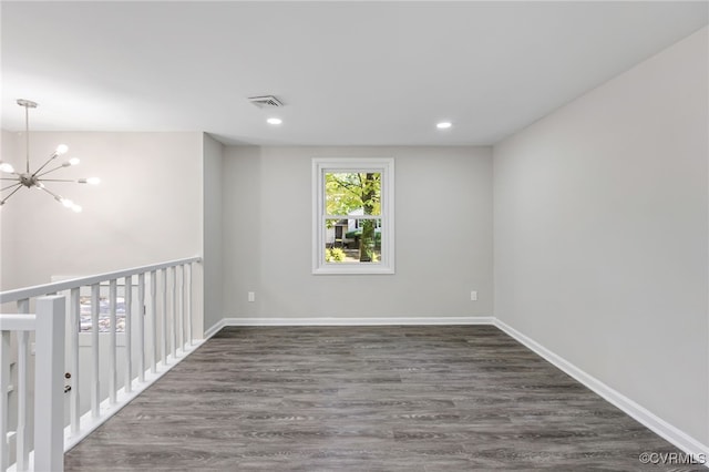 empty room with dark wood-type flooring and a notable chandelier