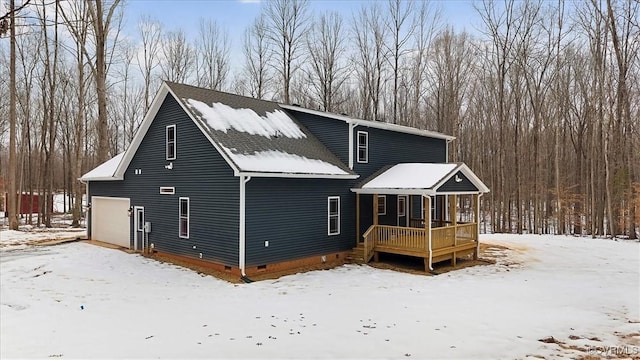 snow covered rear of property with a garage and covered porch