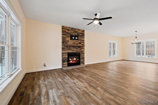 unfurnished living room with a wealth of natural light, ceiling fan with notable chandelier, hardwood / wood-style floors, and a fireplace