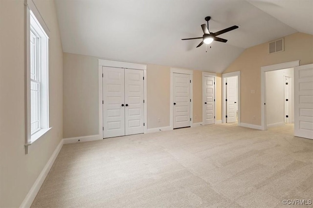 unfurnished bedroom with light carpet, multiple closets, vaulted ceiling, and ceiling fan