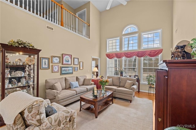 living room with ceiling fan, a towering ceiling, and light wood-type flooring