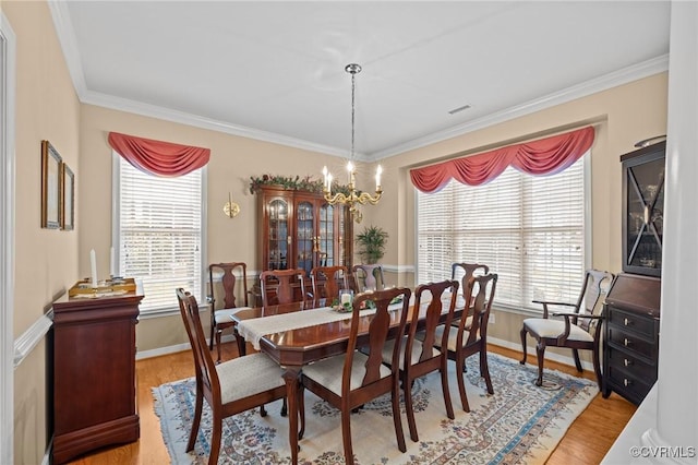 dining area with a notable chandelier, ornamental molding, and light wood-type flooring